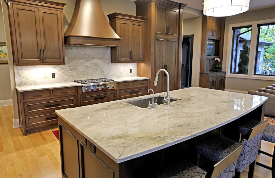 The earthtone veining in the Quartzite island, countertops and full-height backsplash offset the dark wood cabinets and copper range hood in this formal kitchen.