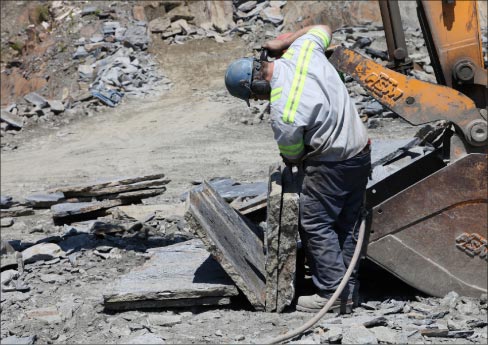 According to Jerry Pratt, their quarry was once the floor of an old ocean basin that’s still being pushed inland and being buckled. Bed lines run at about a 15-degree angle. Four full-time quarriers regularly tend to production, and on the day of this photo, they were splitting schist for patio and wall construction shop, and blocks for the shop.
