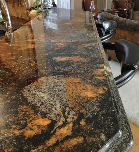 This exotic Brazilian Granite kitchen features a long, two-level expanse of textured stone with a decorative ogee edge. The angled travertine backsplash offsets the dark and lively movement in this beautiful stone.